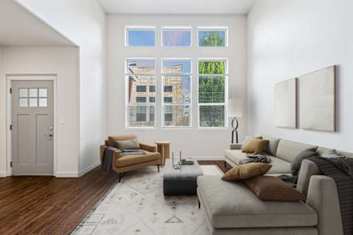 A living room with a grey couch, a brown armchair, and a grey ottoman. at Verraso Village Apartments, Meridian, Idaho
