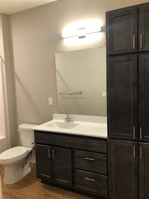 A bathroom with a toilet, sink, and cabinets.
