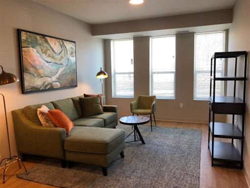 A living room with a green couch, a chair, and a painting on the wall.