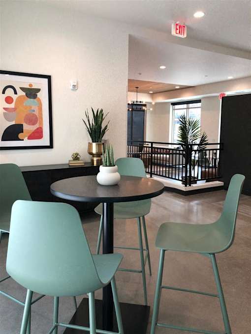 A green chair is in the foreground of a photo with a framed picture of a colorful elephant on the wall.