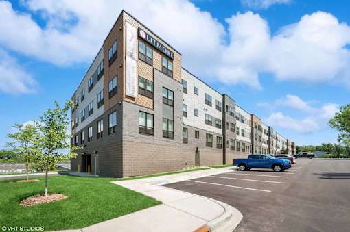 A parking lot is in front of a multi-story brick building.
