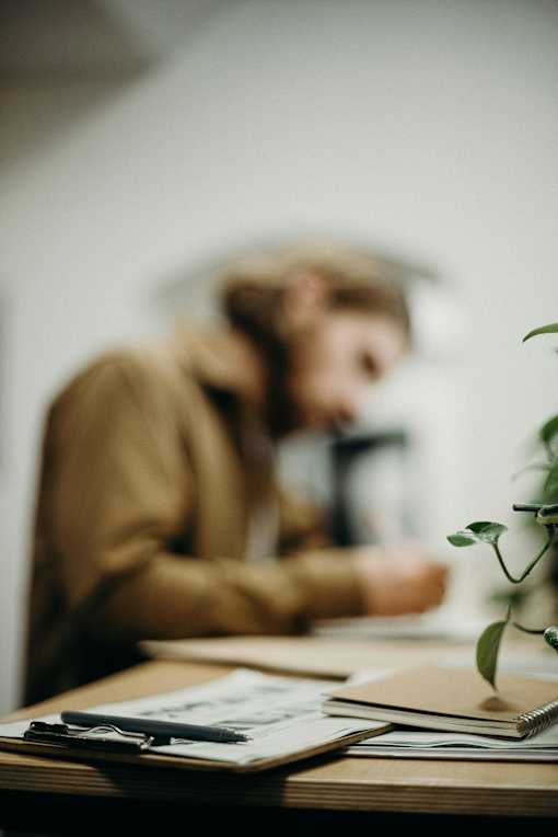 A person is sitting at a desk with a notebook and a pen in front of them.