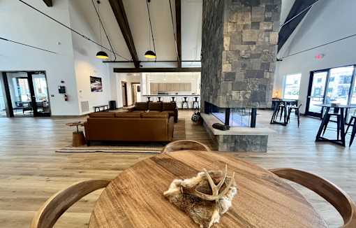 A wooden table with a cloth on it is in the foreground of an indoor space with a stone wall and wooden floors at Silverbrook Apartments Apartments, Ridgeland, Kalispell
