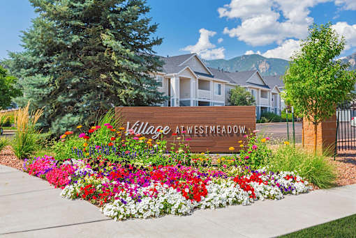 A sign that says Village at Westmeadow in front of some houses.