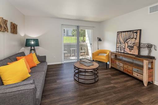 A living room with a grey couch, yellow pillows, a round table, and a wooden bench.