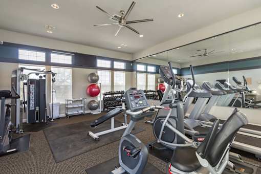 A gym with a variety of equipment including treadmills, weights, and a ceiling fan.