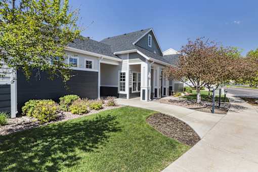 A house with a grey roof and white trim is surrounded by a well-manicured lawn and trees.