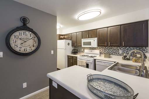 A kitchen with a white counter top and a large clock hanging on the wall.