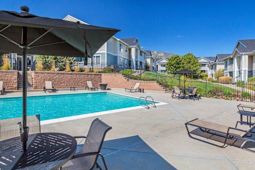 A black umbrella is on a table next to a pool.
