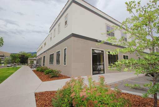A modern building with a grey and white exterior and a landscaped front yard.