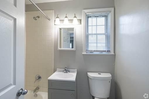 A bathroom with a white sink, toilet, and a mirror above a light switch.