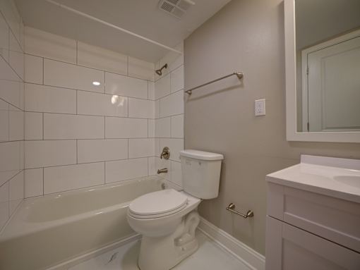 A white toilet sits in a white tiled bathroom.