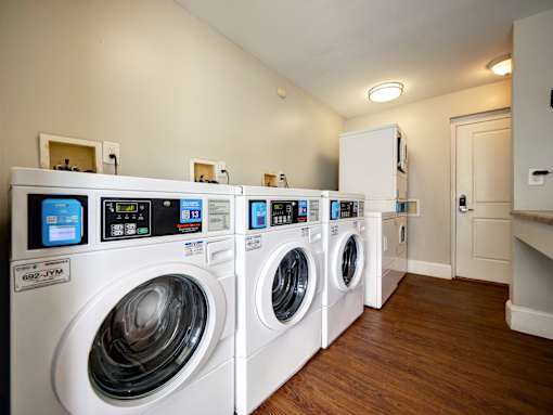 A row of white front load washing machines are lined up in a laundry room.