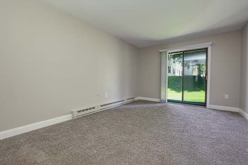 A room with a carpeted floor and a sliding glass door leading to a backyard.