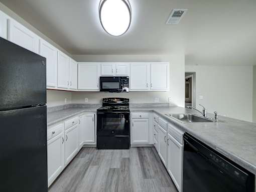 A black fridge sits in a kitchen with white cabinets and a black stove.