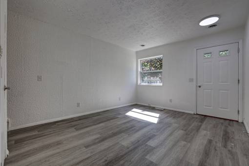 A room with a white door and a window with a view of trees outside.