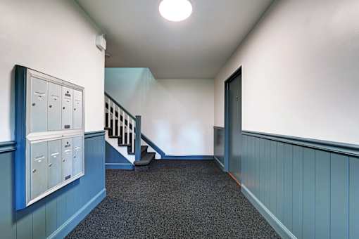 A hallway with a staircase and mailboxes on the wall.