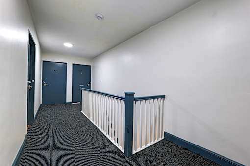 A hallway with a white railing and dark carpet.
