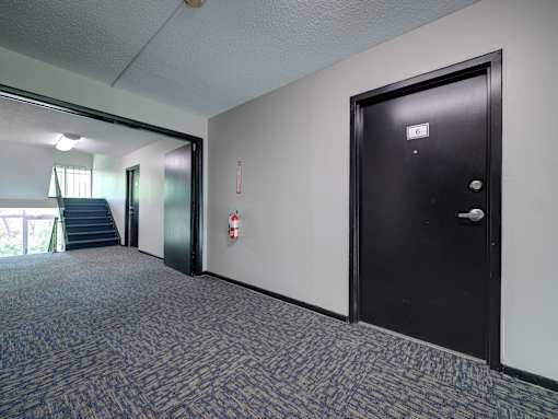 A hallway with a black door and a red fire extinguisher on the wall. at Highland Club Apartments, Watervliet, NY 12189