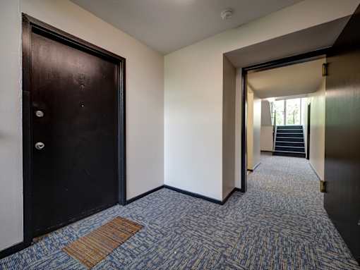 A hallway with a carpeted floor and a door on the left.  at Highland Club Apartments, Watervliet, NY 12189