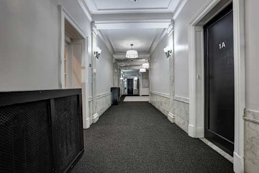 A long hallway with a black door on the right and a black speaker on the left.
