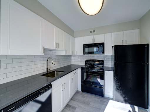 A black refrigerator sits in a kitchen with white cabinets and a black dishwasher.