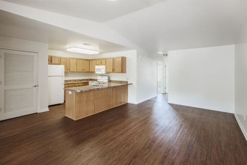an empty living room and kitchen with wood floors and white walls