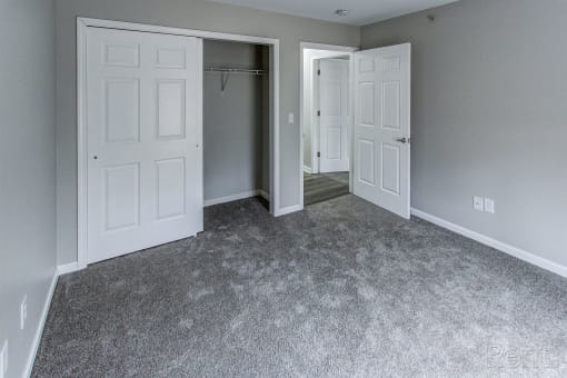 an empty bedroom with white doors and a carpeted floor