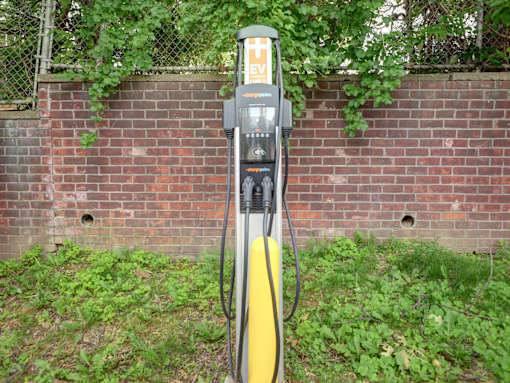 A yellow and black electric vehicle charging station sits in front of a brick wall.
