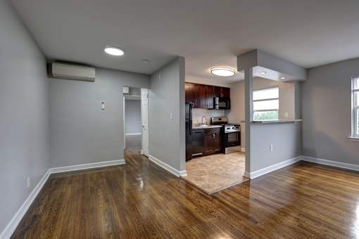 A room with wooden floors and a kitchen area in the background.