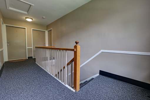 A hallway with a carpeted floor and a wooden railing.