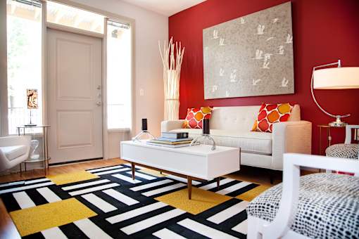 A white sofa with red and orange pillows sits in a room with a red wall and a white chair.