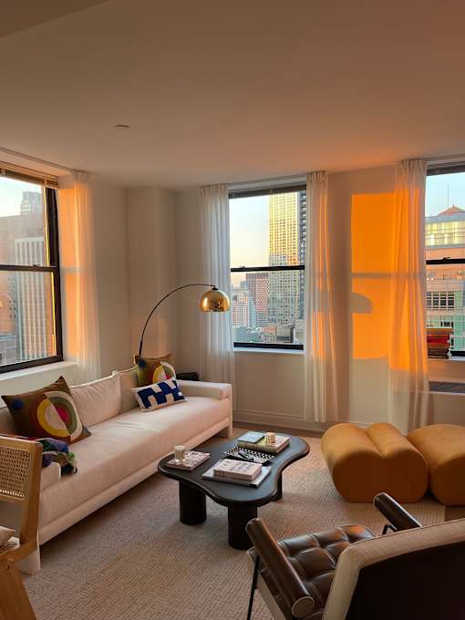 A living room with a white couch, a coffee table, and a large window with a view of the city.