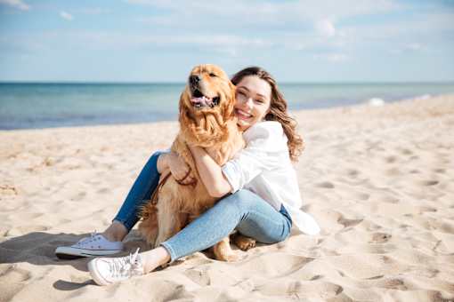 A woman is sitting on the beach with her dog.