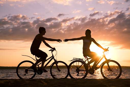 Two people riding bicycles on the beach at sunset.
