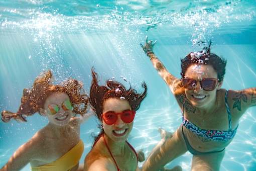 Three women are swimming underwater in a pool.
