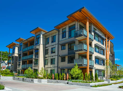 A modern multi-story residential building with balconies and a mix of grey and wood accents.