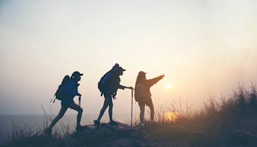 Three hikers with backpacks are silhouetted against the sunset.