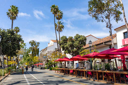 A street with red umbrellas and palm trees.