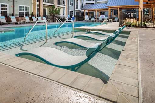 a swimming pool with four chaise lounges and a building in the background