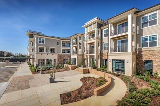 an exterior view of an apartment complex with a walkway and landscaping