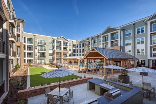 an outdoor patio with tables and umbrellas in front of an apartment complex