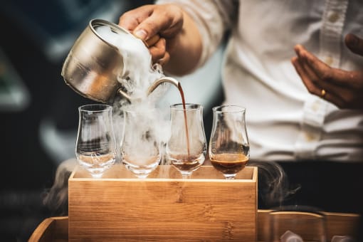 a man in a white shirt pours whisky into glasses in a wooden box