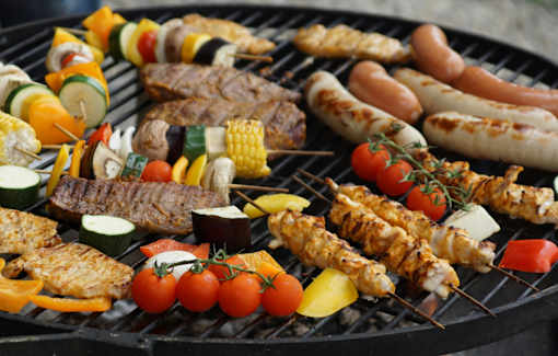 A variety of meats and vegetables are being grilled on a barbecue.
