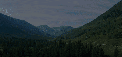 a view of the mountains in the distance with a road and trees in the foreground