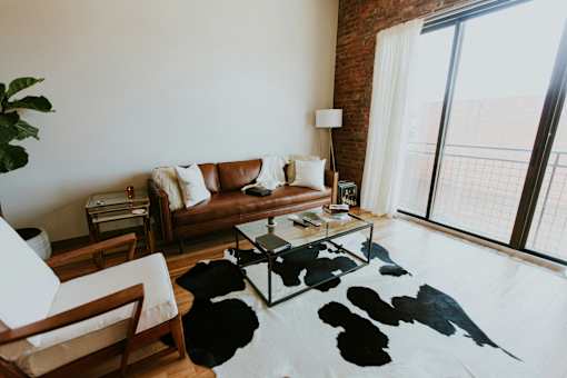 A living room with a white couch, a wooden chair, a black and white cowhide rug, and a large window.