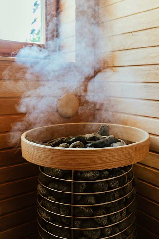 Steam rising from a wooden hot tub filled with black stones.