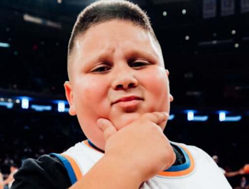 A young boy in a white and orange jersey is sitting in a stadium.