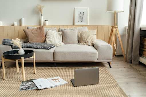 A modern living room with a grey sofa, a round table, and a laptop on the carpet.