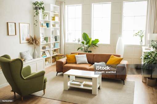 A living room with a green armchair, a brown sofa, a white coffee table, and a bookshelf with plants.